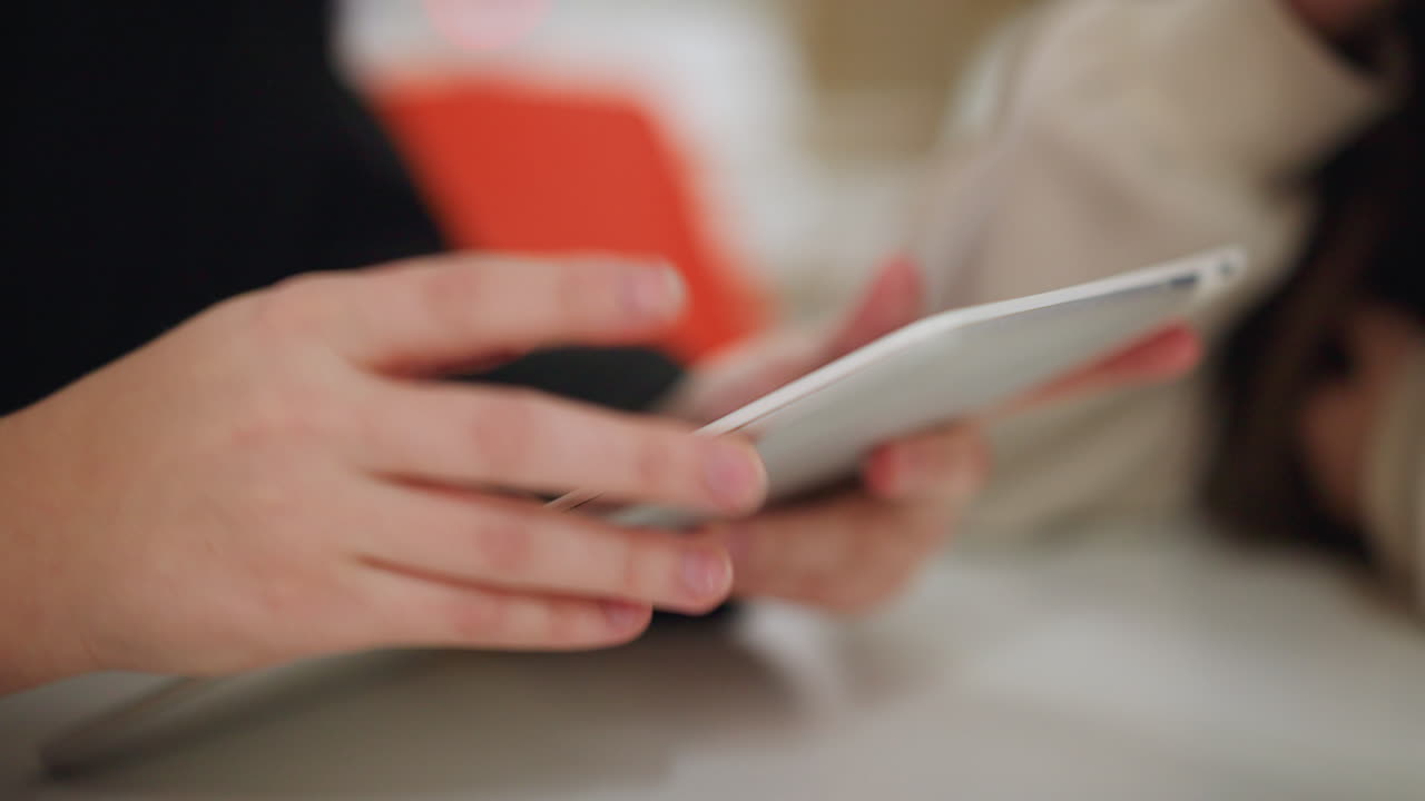 Primo piano di una persona che tiene in mano un tablet mentre un'altra beve da una tazza, dettaglio di un'interazione in ambienti interni tipica di uno stile di vita casual, attenzione su mani, tecnologia e comunicazione moderna