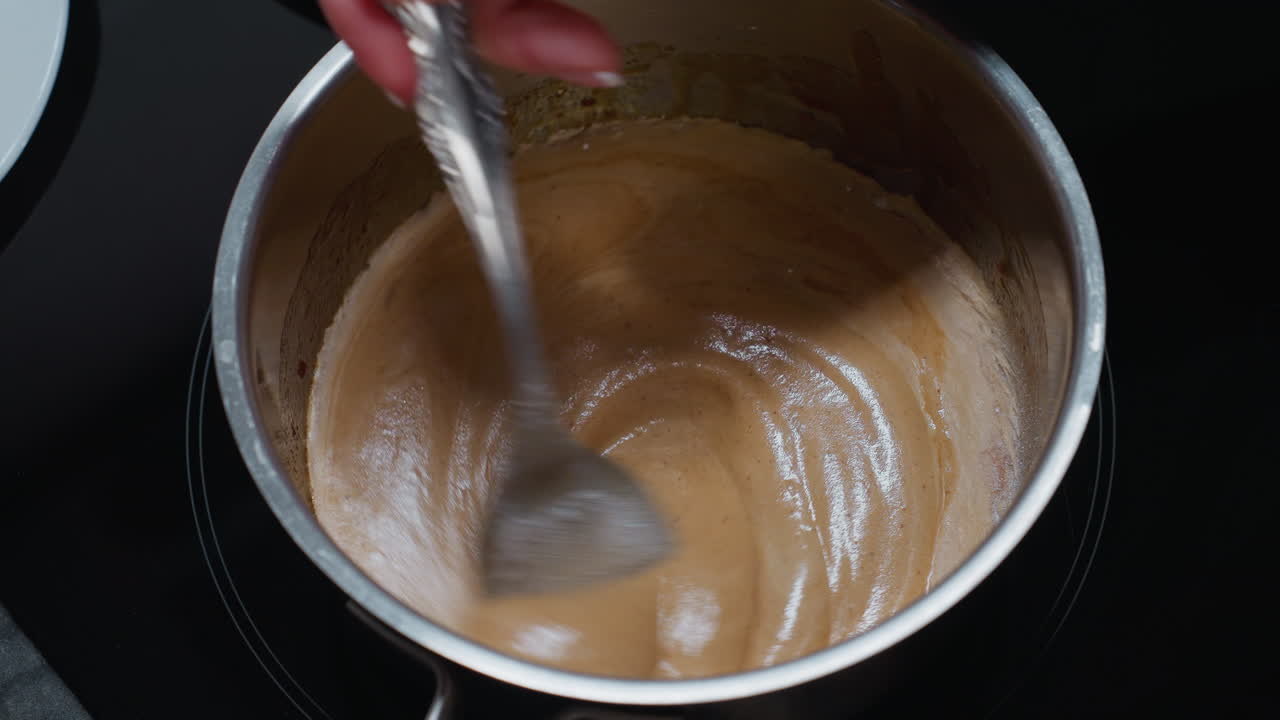 primer plano del cocinero agitando el pap liso en la estufa eléctrica, creando una textura cremosa con una vista parcial de un plato blanco, la avena gruesa se gira mientras se prepara cuidadosamente