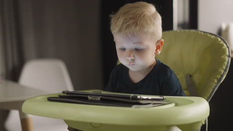 tranquil little boy watches video via tablet in high chair