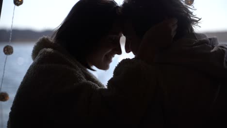 a young couple in love put their heads together in the back of a caravan by a lake.