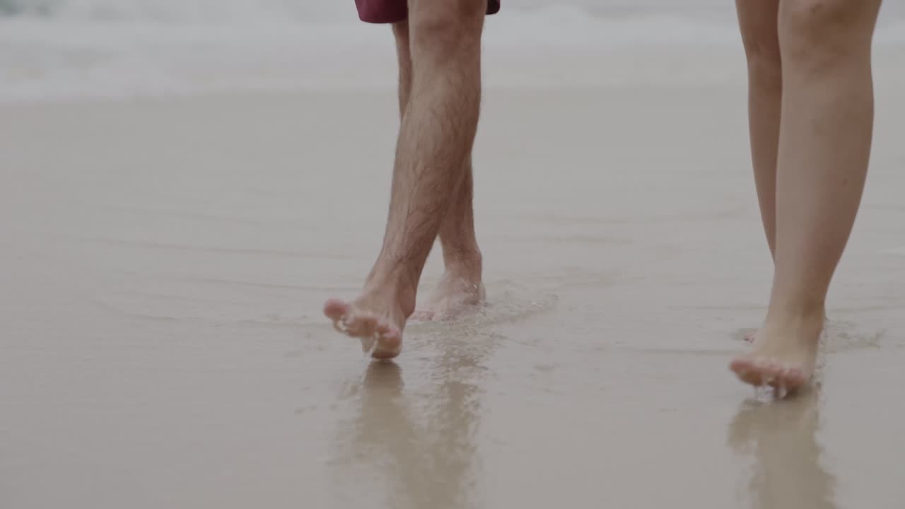 Two people walking barefoot in shallow water on a sandy beach