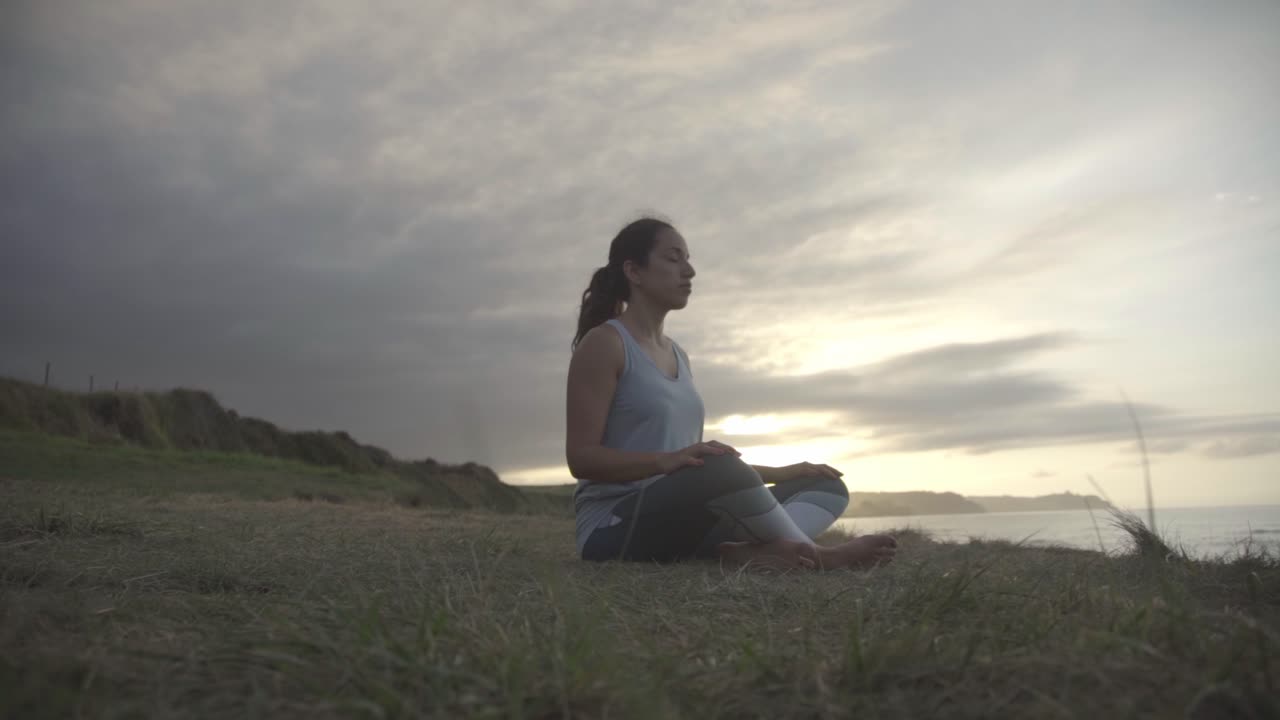 mujer fitness meditando en un ambiente tranquilo, puesta de sol en el fondo, cielo nublado, asturias, españa, cámara lenta