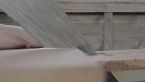 Workman-hand-using-manual-saw-to-saw-piece-of-wood-on-workbench
