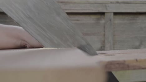 workman hand using manual saw to saw piece of wood on workbench