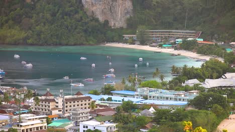 the port and pier of koh phi phi with longtail boats and the beautiful turquoise beach with hotels nearby in thailand