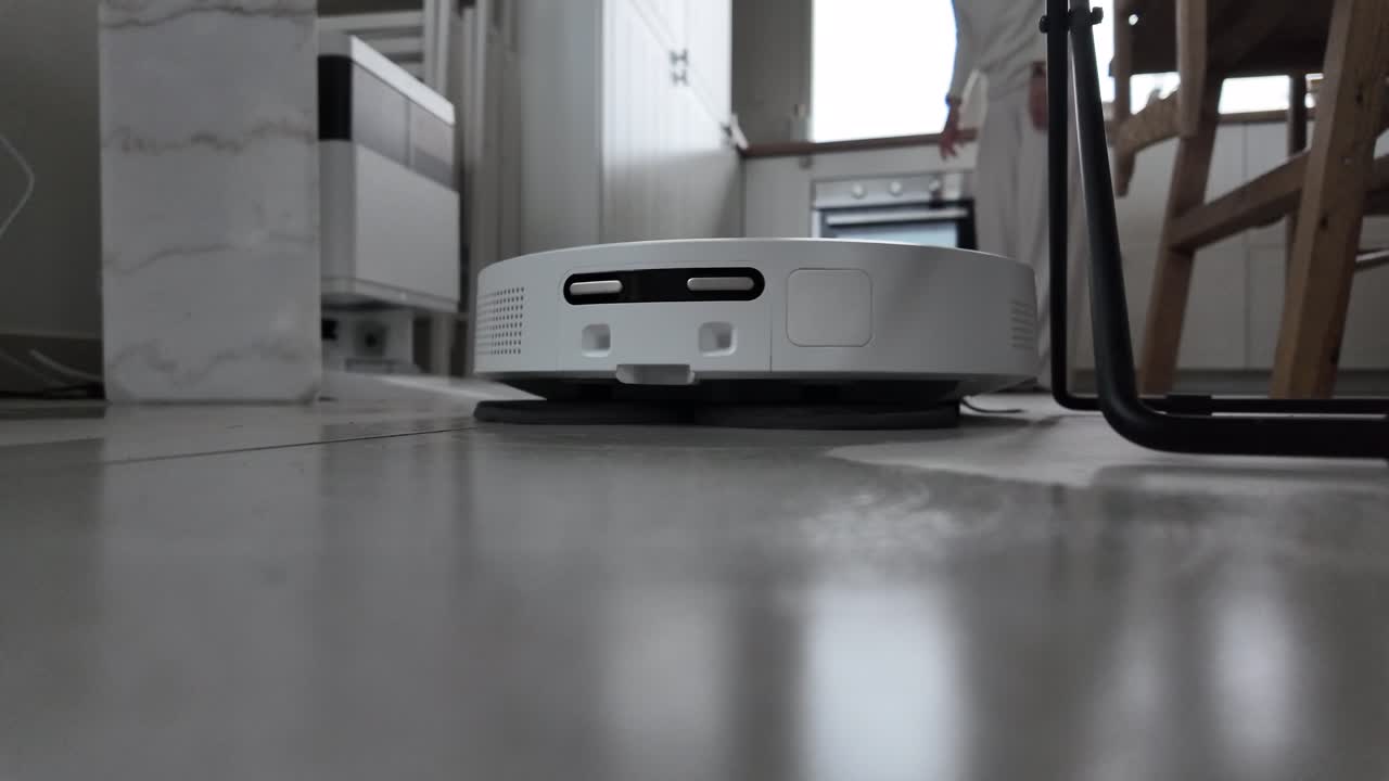 Robotic floor cleaner moving across a tiled indoor surface in a low-angle view