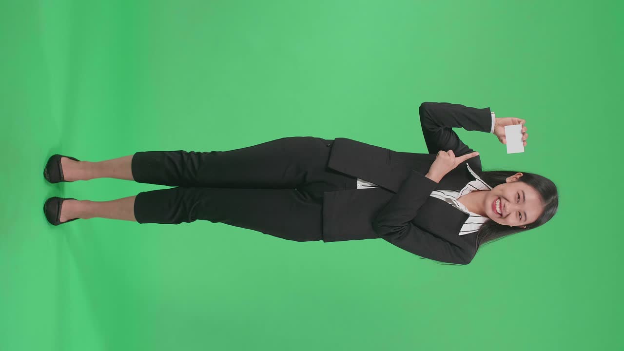 Full Body Of An Asian Business Woman With Smile Pointing A White Card In Hand While Standing In Front Of Green Screen
