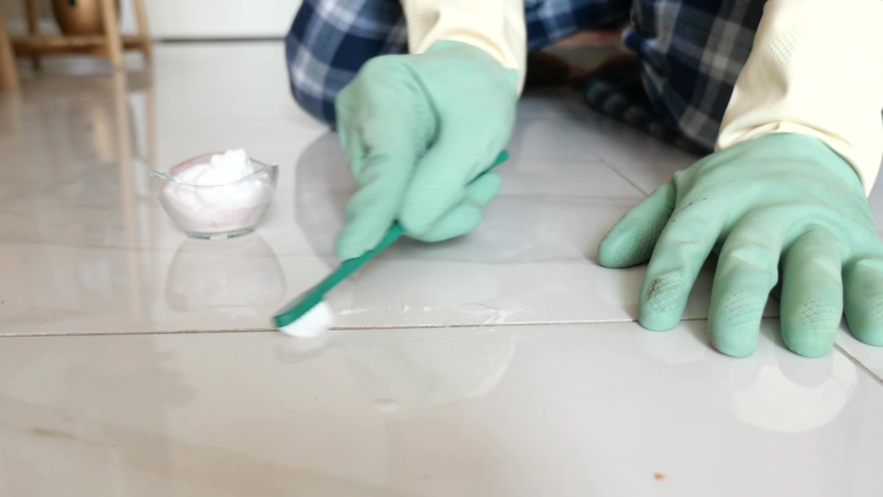 Person Scrubbing Tile Grout with Toothbrush and Cleaning Powder