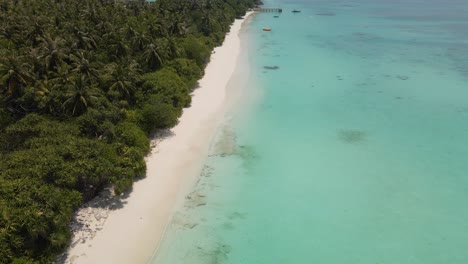 Drone-flight-over-the-coast-of-the-Maldivian-island,-blue-water-against-a-beautiful-sky-and-a-pier-in-the-water