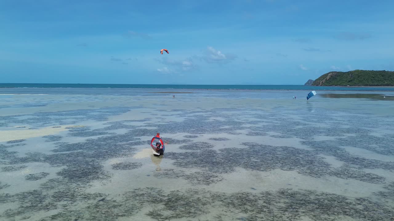 Aerial drone video of small fishing boats near the sandy shore of Thong Sala Beach with kitesurfer pratctice in turquoise shallow water in the background