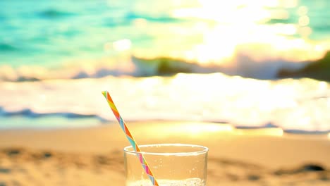 glass of drink on sandy beach with ocean view at sunset