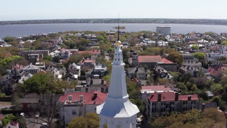 Toma-Panorámica-Aérea-De-Paralaje-De-La-Aguja-En-La-Cima-De-La-Iglesia-De-San-Miguel-En-El-Histórico-Barrio-Francés-De-Charleston,-Carolina-Del-Sur.