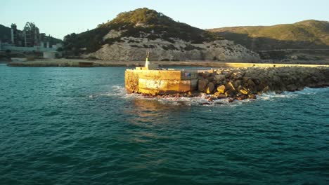 Pintoresca-Costa-De-Garraf-Con-Rompeolas-Rocoso-Y-Distante-Fábrica-De-Cemento-Bajo-Un-Cielo-Despejado