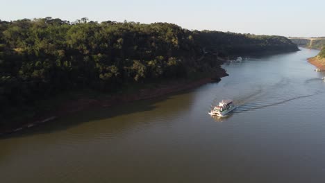 tourist boat sailing along navigable iguazu river at border between argentina and brazil at sunset