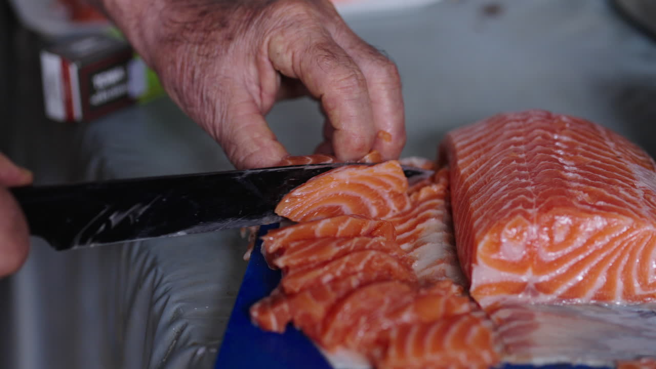 Slicing fresh raw salmon by hand with a knife for sashimi preparation. Close-up