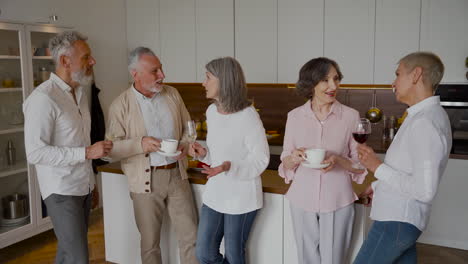 Gruppe-Fröhlicher-älterer-Freunde,-Die-In-Der-Küche-Lachen-Und-Wein-Und-Kaffee-Trinken-1