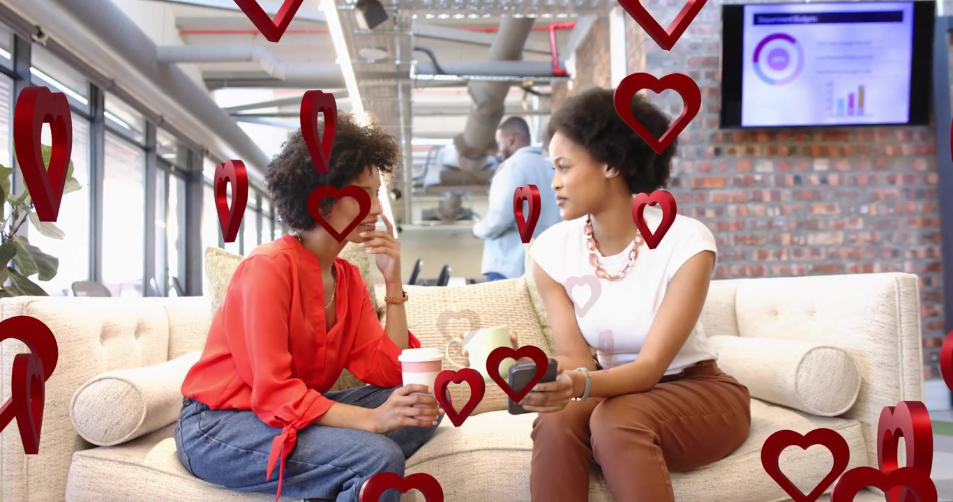 Two marketers chatting over coffee in lounge pulling phone to share post with floating hearts