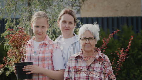 portrait of mother, daughter and granddaughter - together in their garden, holding flower pots for planting