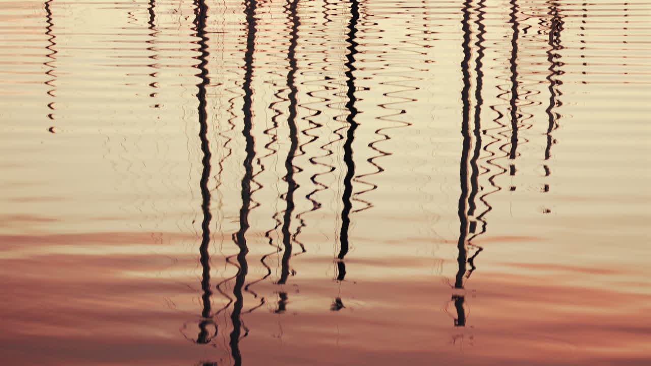 Reflections of boat masts distorted on still marina water during sunset