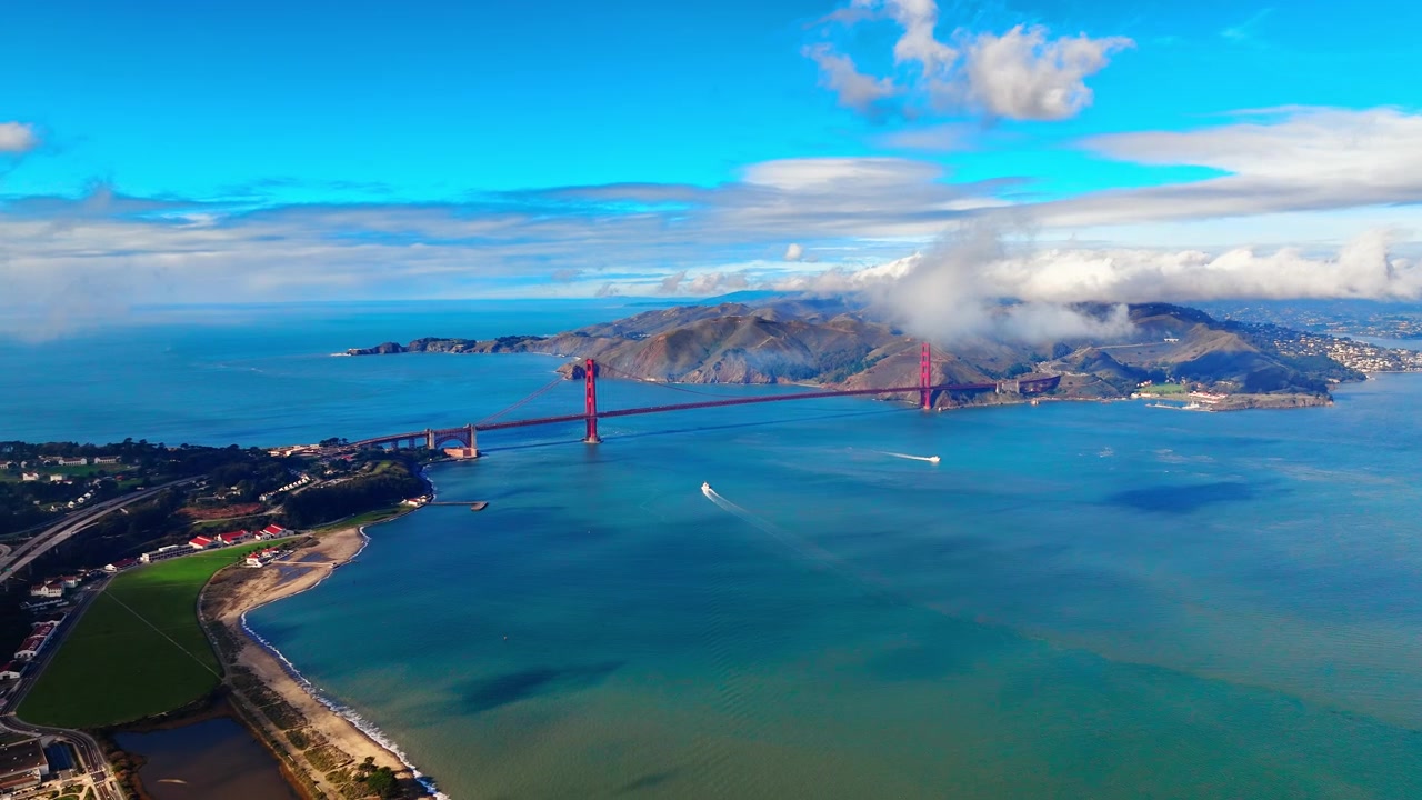 Ponte Golden Gate che attraversa la baia con le promontori di Marin e una barca sotto, San Francisco. Iconico ponte sospeso rosso che attraversa acqua blu-verde, promontorio costiero e strato di nuvole dietro
