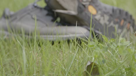 Close-up-of-blades-of-grass-moving-in-the-wind-with-discarded-hiking-shoes-in-the-background