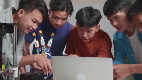 group of young asian boys with 3d printing comparing a cyborg hand to the pictures on a laptop while working at home