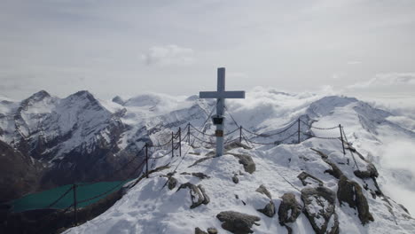 Toma-De-Drones-Que-Muestra-La-Cruz-De-La-Cumbre-Sagrada-En-El-Pico-Nevado-De-La-Montaña-Alp-Iluminada-Por-El-Sol---Toma-En-órbita