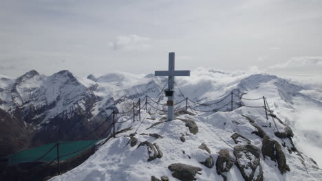 toma de drones que muestra la cruz de la cumbre sagrada en el pico nevado de la montaña alp iluminada por el sol - toma en órbita
