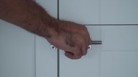 close up of man unlocking the latch on a door of a modern white house