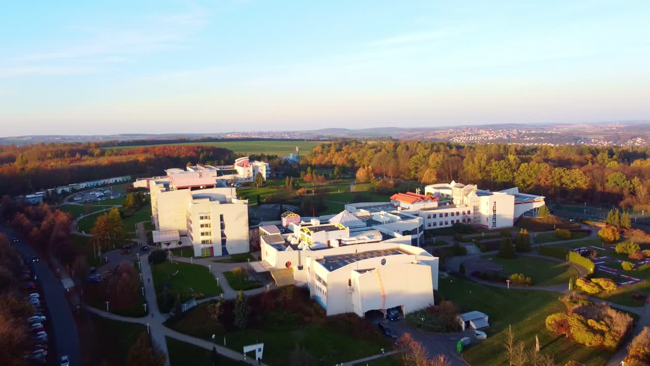 Aerial pullback ascend of historic wellness building in autumn, surrounded by scenic Czech landscape and colorful foliage