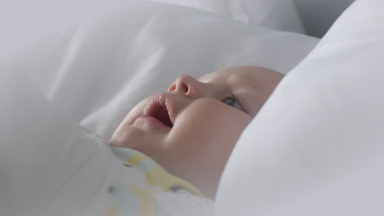 Dolce primo piano di un bambino che gioca e sorride in lenzuola bianche pulite e morbide.