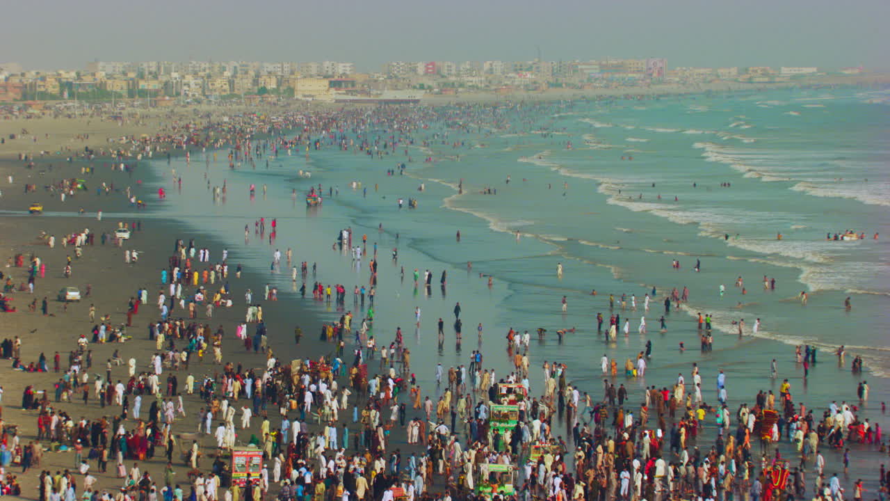 해변과 도시의 긴 원근감이 보이는 아름다운 푸른 바다가 있는 바다 전망 해변에서 함께 움직이는 해변 파도와 드론, 수많은 군중이 즐기기 위해 왔습니다.
