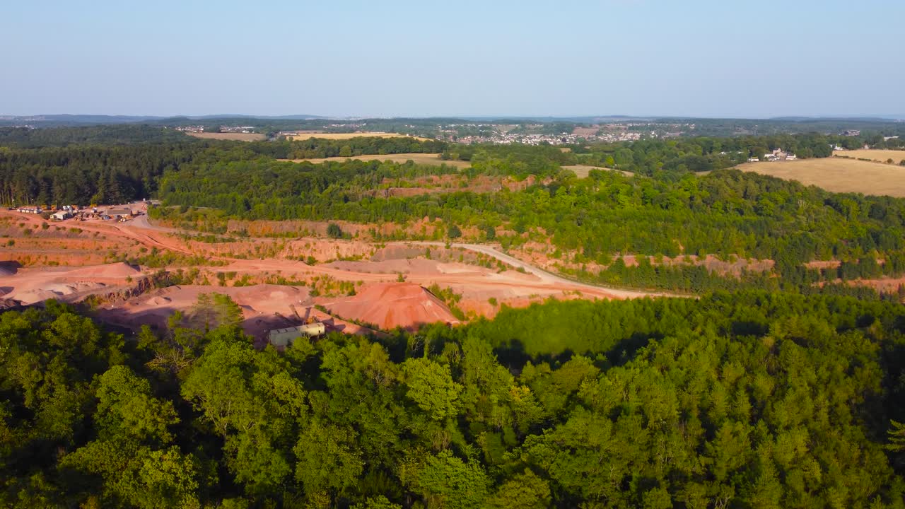 Sideways Aerial View Over Deep Quarry Surrounded by Trees and Fields in British Countryside. Heavy Mining Excavating Industry Surrounded by Natural Environment