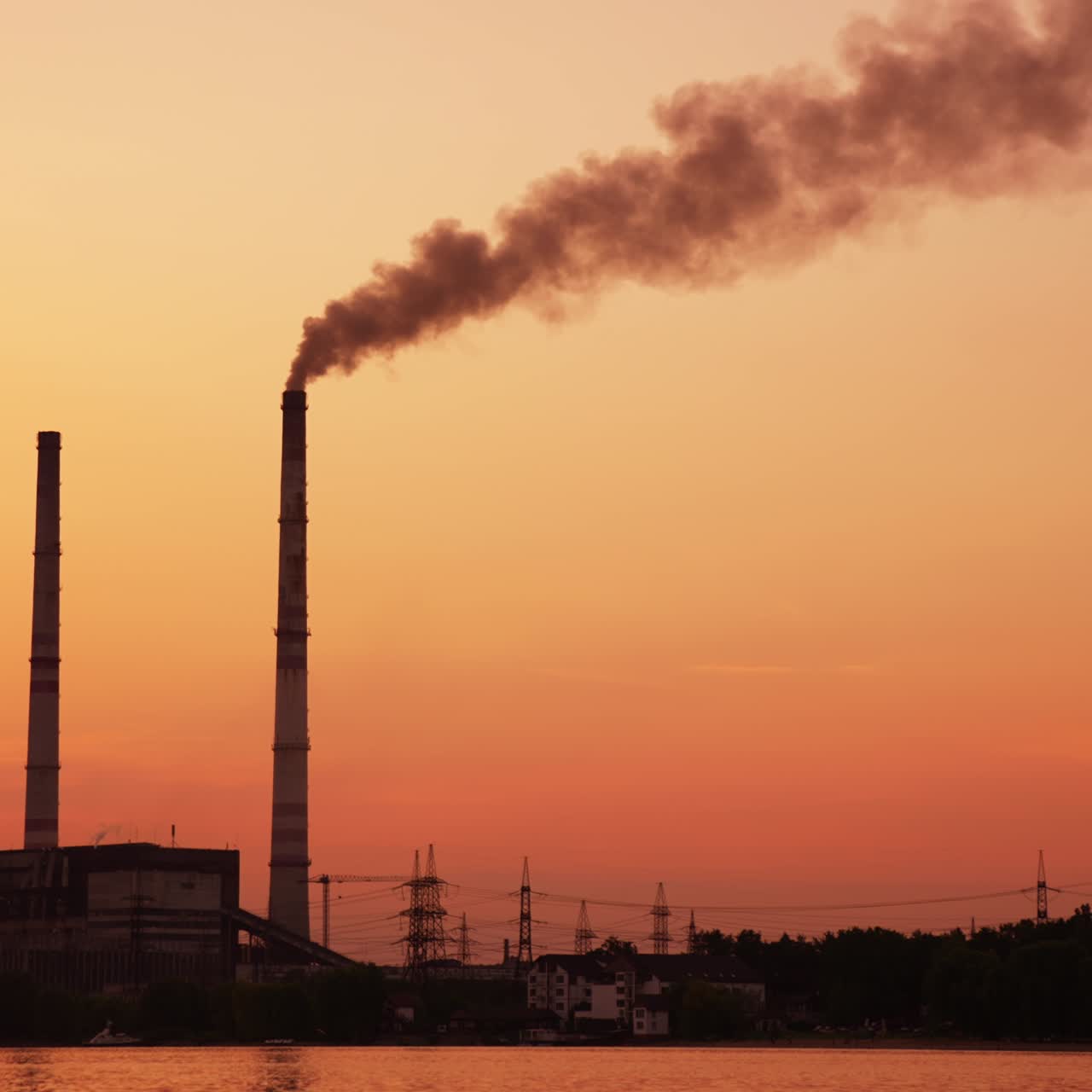 Orange picturesque scenery of a plant at sunset. Two high pipes over the industrial zone one of which produces smoke