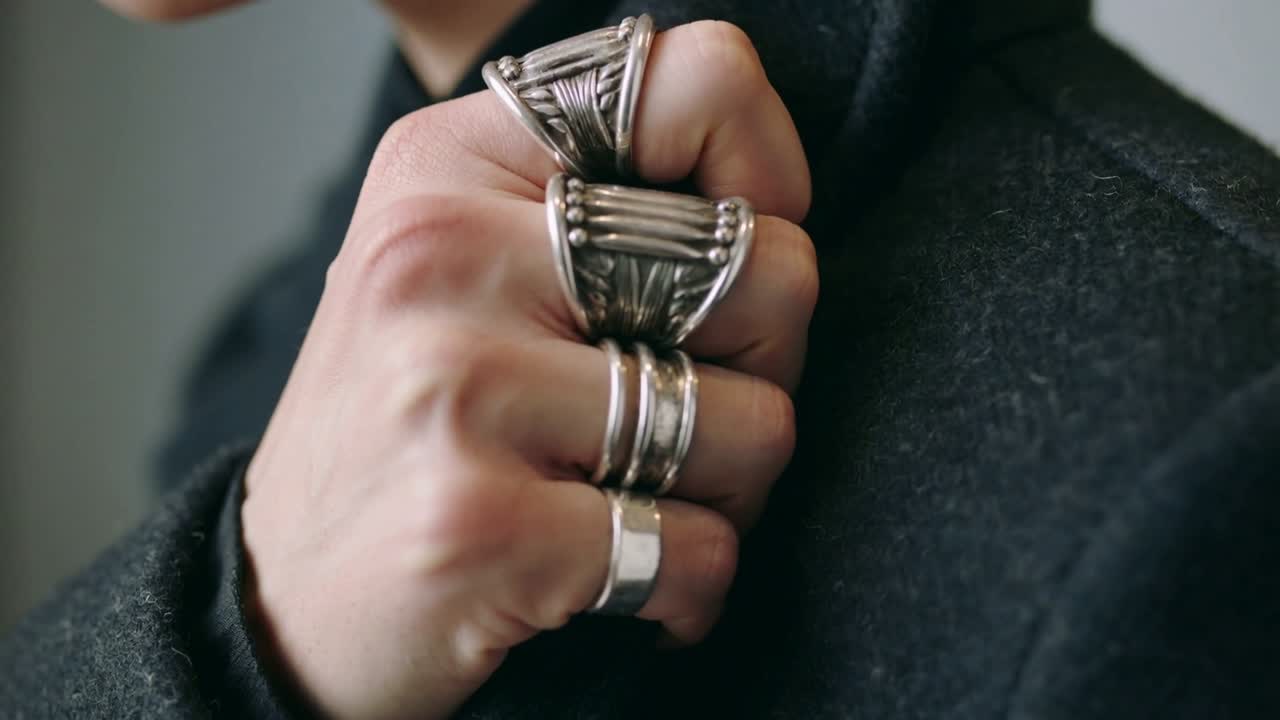 Uomo che appoggia il pugno sul bavero della giacca e ruota la mano, mettendo in evidenza anelli d'argento per una sfilata di moda