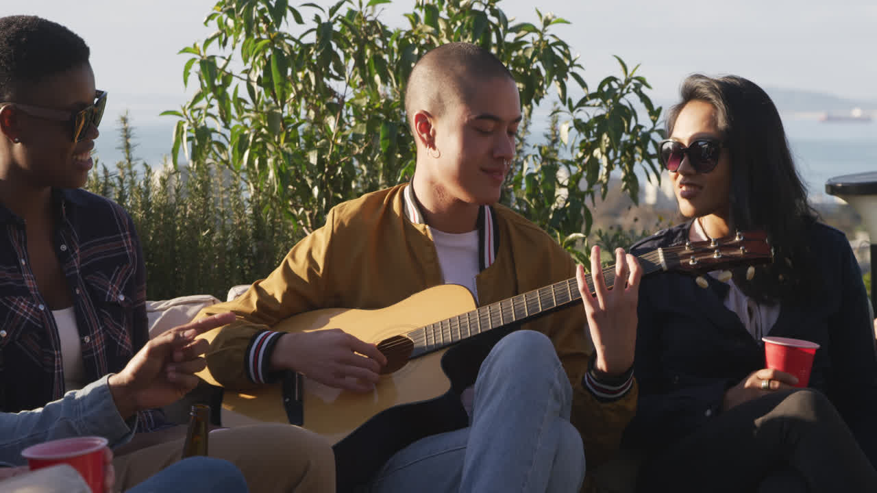 Giovane uomo che suona la chitarra su un tetto con i suoi amici