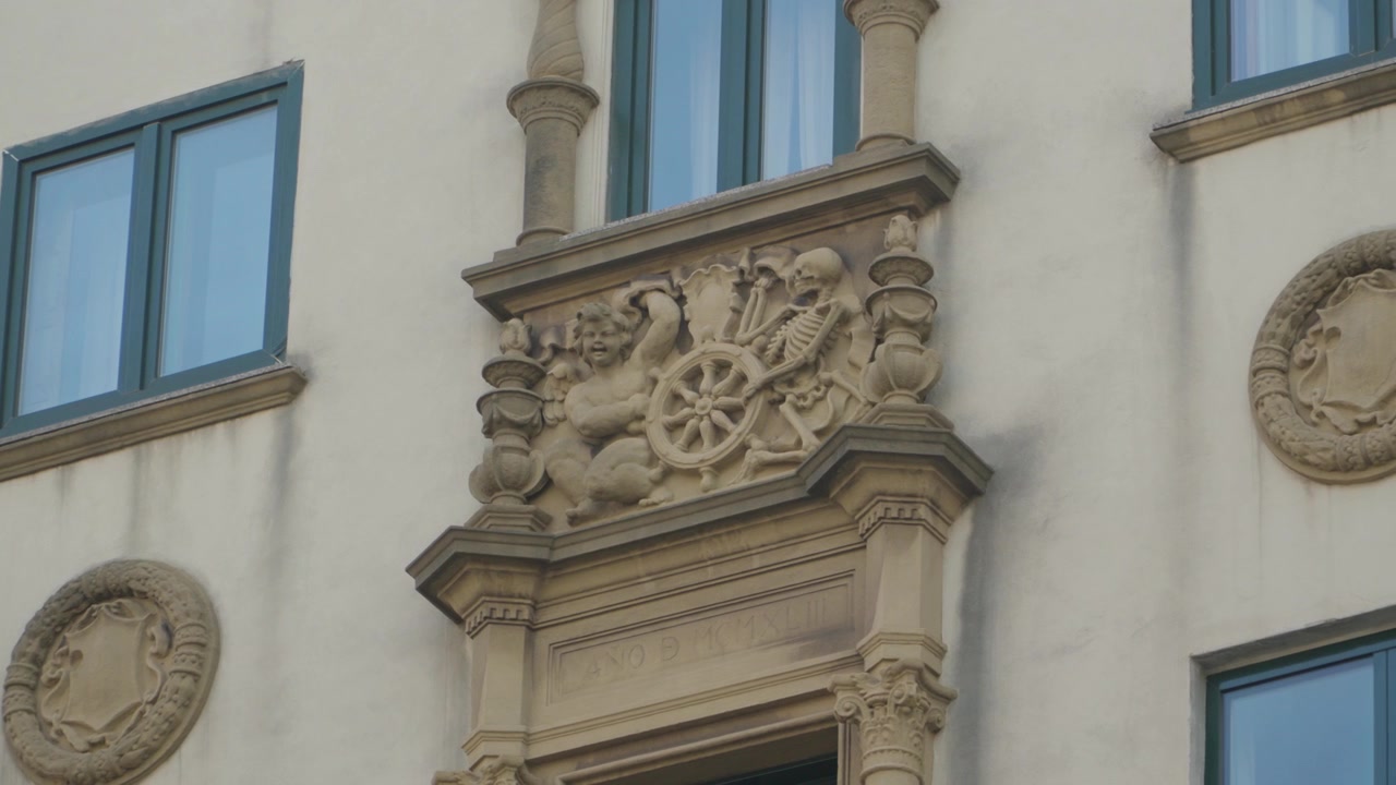 Stone carving on an old building depicting a skeleton and a cherub, a memento mori allegory