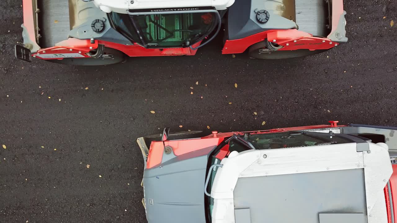 Top view of heavy machinery at roadworks. Two asphalt compactors working on different sides of the road. Camera moves bottom up.