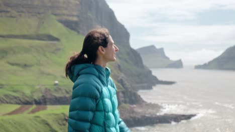 una mujer con una chaqueta azul azul disfruta de una serena vista costera en gásadalur, islas feroe
