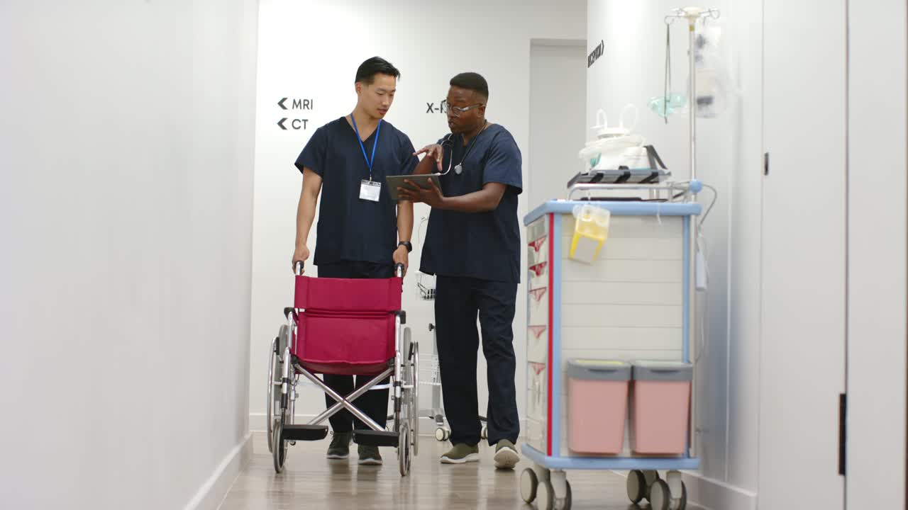 Personale maschile di diverse etnie che consulta un tablet dopo l'arrivo di un collega con una sedia a rotelle rosa, pianificando le scansioni.