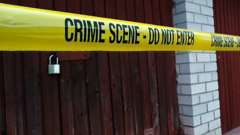 close up of yellow police crime scene tape stretched across entrance of old wooden garage door marking crime scene or suspected break in. ongoing criminal investigation, warning tape flutters in wind