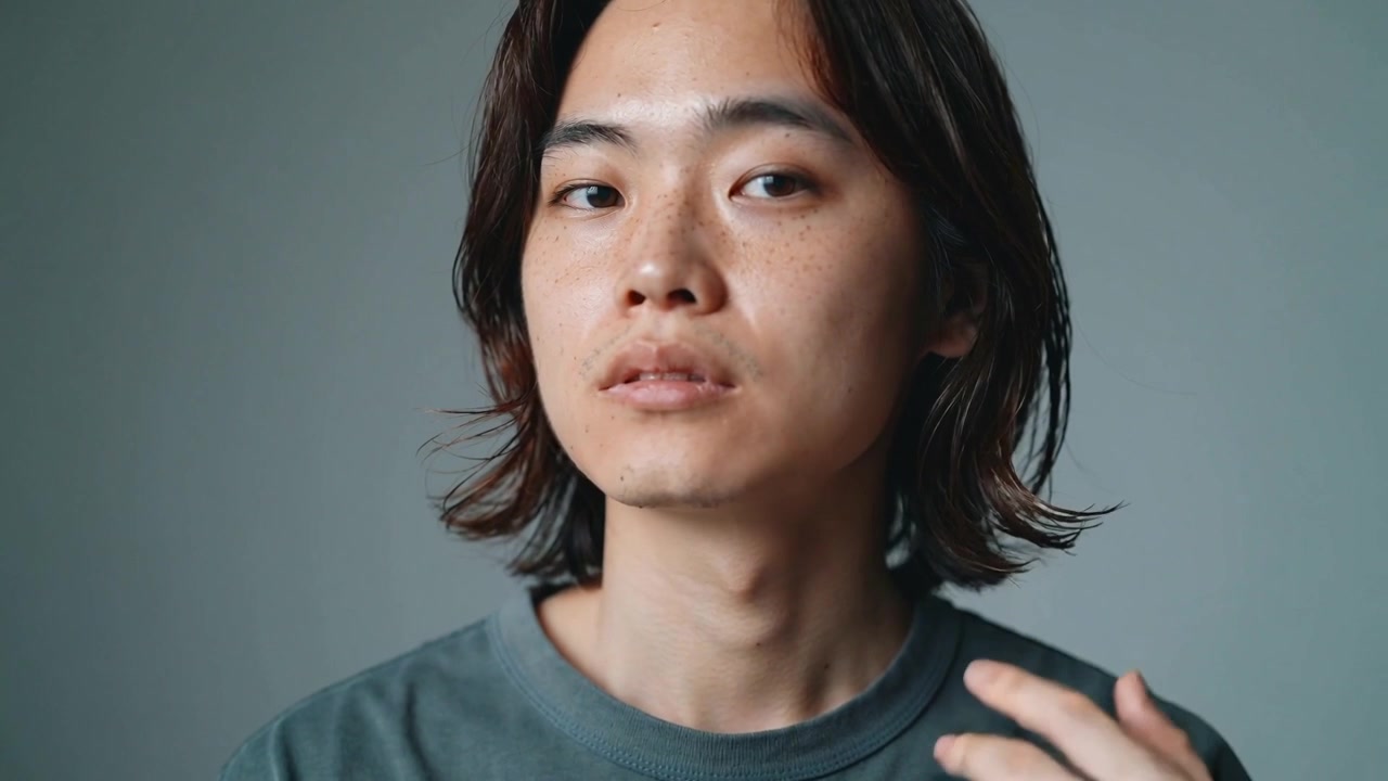 Pria Asia menyisir rambut, menanggapi isyarat kamera, menyesuaikan kepala di studio, mengenakan kaus abu-abu.