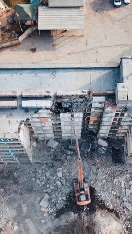 natural disaster demolition building. excavator at a construction site disassembles construction debris. aerial view. vertical video