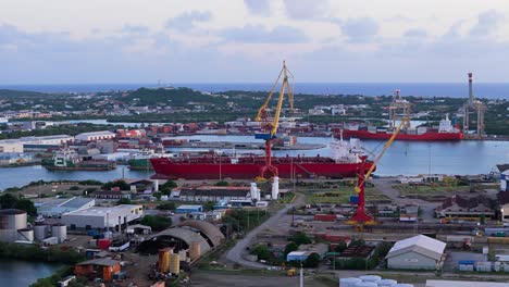 industrial seaport cranes above tanker transit ship docked in port at sunset on island