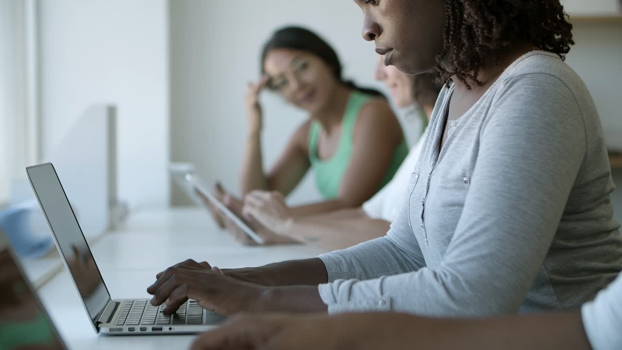 vista lateral de una mujer joven concentrada escribiendo en una computadora portátil
