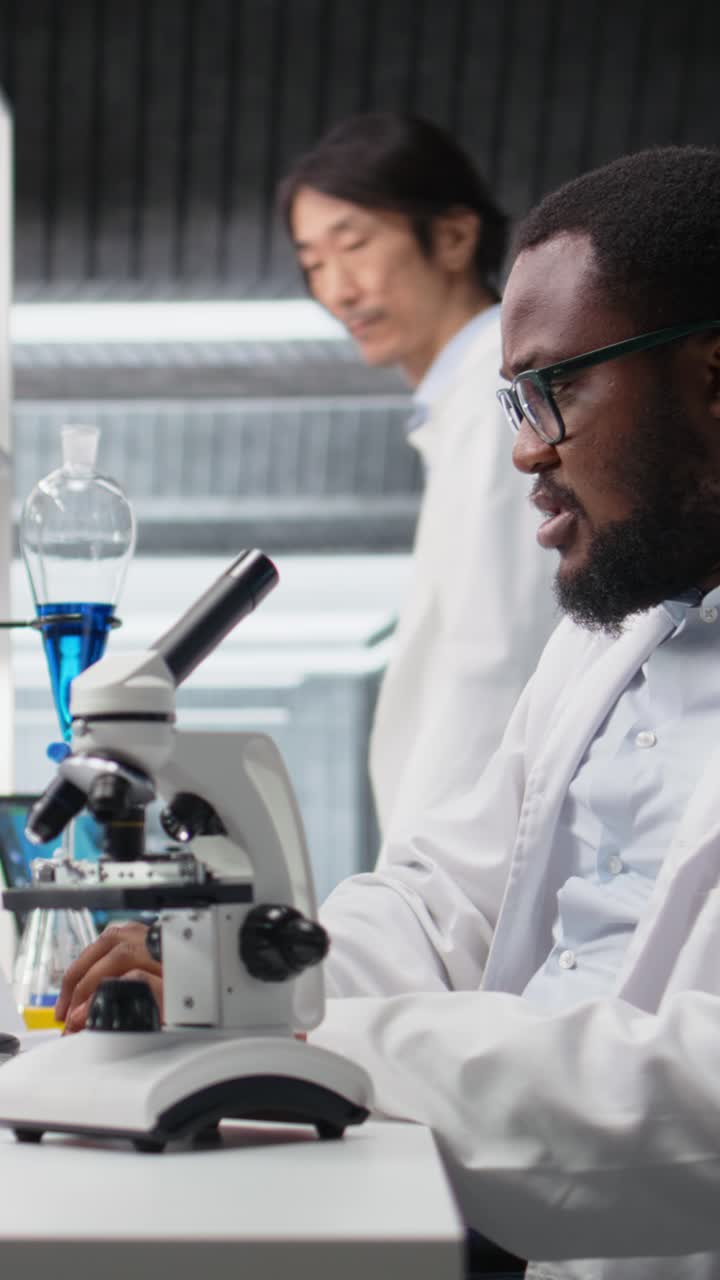 Vertical video Microbiologist in lab inspects slide using optical device, analyzing on PC