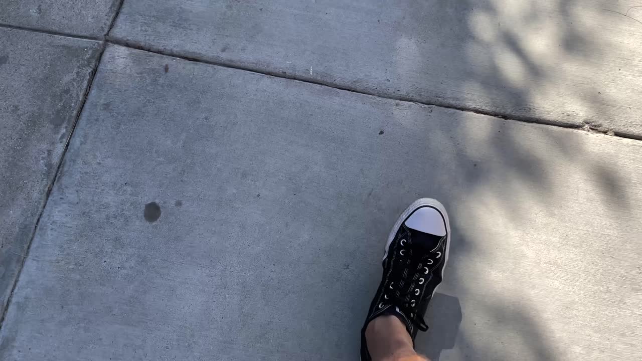 Man walks on sidewalk wearing tennis shoes, looking down POV
