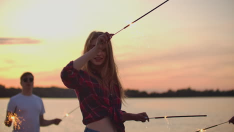 La-Bella-Mujer-Con-Cintura-Desnuda-Baila-Con-Grandes-Luces-De-Bengala-En-La-Costa-Del-Río.-Esta-Es-Una-Agradable-Tarde-De-Verano-En-La-Fiesta-Al-Aire-Libre-Bajo-El-Atardecer-Naranja.