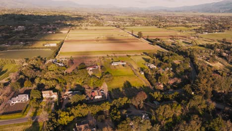 Imágenes-Aéreas-De-Casas-Y-Granjas-De-Santa-Ynez-En-La-Hora-Dorada,-Campos-Verdes-Y-Cultivos-Con-Montañas-En-El-Horizonte