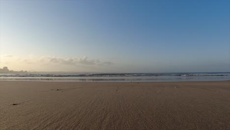 Ruhige-Aufnahmen-Vom-Strand,-Dem-Meeressand-Und-Den-Ruhigen-Kleinen-Wellen,-Die-Im-Hintergrund-Unter-Einem-Himmel-Mit-Wenigen-Wolken-Brechen